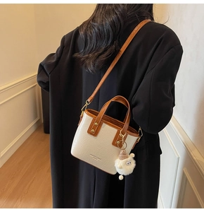 Close-up of beige pleated bucket bag featuring brown straps and a plush monster charm