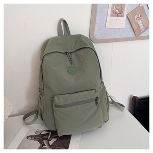 Vue détaillée d'un sac à dos en nylon vert sauge avec poche frontale et logo rond
