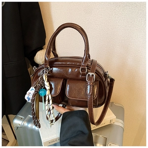 Dettaglio borsa in pelle lucida marrone scuro con corda intrecciata e ciondolo blu