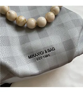 Dettaglio della borsa a quadri grigi con manico di perle e logo in stile vintage