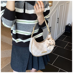 Detailed shot of white checkered crescent bag with plush bunny charm and golden logo
