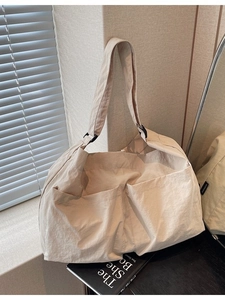 Minimalist beige nylon tote bag with front pockets and adjustable strap shown in sunlight