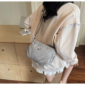 Detailed view of light grey nylon crossbody bag with colorful jacquard strap worn by model
