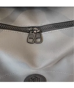 Detail of dual black metal zippers and woven fabric texture on a grey travel bag