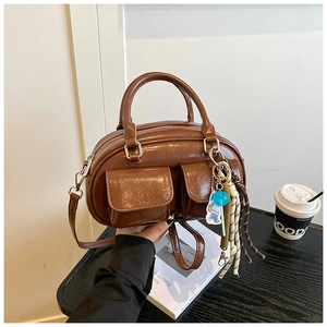 Dettaglio borsa Boston marrone vintage con tasche a patta e ciondolo intrecciato sul tavolo