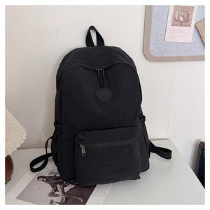 Sac à dos noir minimaliste avec logo rond sur un bureau blanc dans un décor de chambre