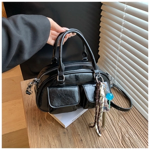 Dettaglio borsa Boston nera lucida in ecopelle con ciondoli decorativi e due tasche frontali