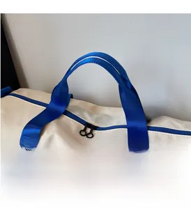 Detailed close-up of reinforced blue handles and durable zippers on the cream travel bag