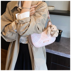 Detail of pink plaid crescent bag with cute plush rabbit charm on stylish woman