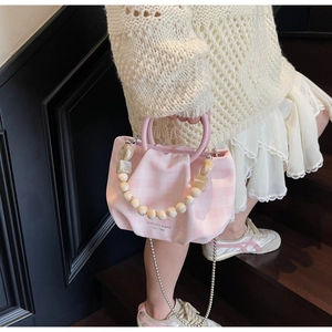 Borsa a quadretti rosa con dettagli di perle portata da una modella su scale in legno