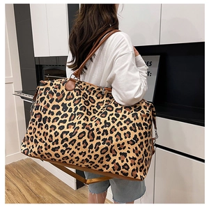 Spacious leopard print duffle bag with leather handles shown on shoulder for travel