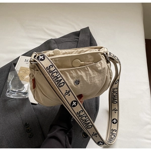 Detail of beige nylon crossbody bag featuring wide logo strap and silicone zipper pull