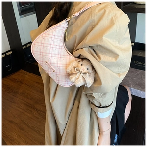 Detail of pink plaid crescent bag worn by model with a white plush bunny charm accessory