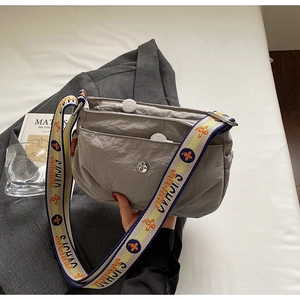 Detail of grey nylon crossbody bag featuring multiple zipper pockets and wide woven strap
