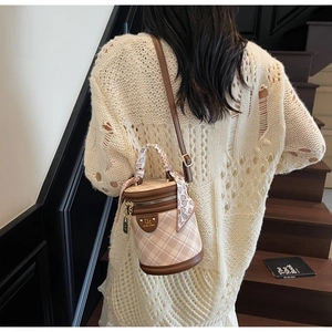 Detail of a vintage cylinder bucket bag featuring beige plaid and brown leather accents