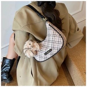 Close-up of crescent plaid bag with leather trim and plush rabbit charm on a model