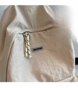 Detail of beige nylon backpack featuring MACHUGE woven label and textured fabric