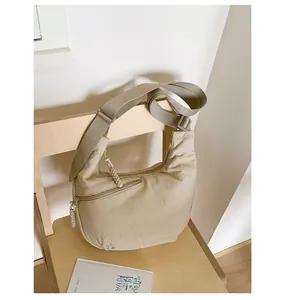 Detail of light beige crescent crossbody bag with front zipper and woven puller on a chair