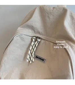 Detail of smooth metal zipper with cord pull and brand label on beige nylon backpack