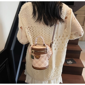 Detail of beige quilted bucket bag with silk scarf handle and leather trim on a model