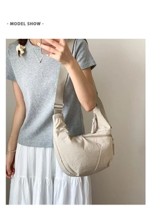 Detailed view of beige crescent bag worn crossbody with adjustable nylon shoulder strap