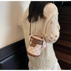 Quilted bucket bag with silk scarf detail and golden logo worn by a model in casual knitwear