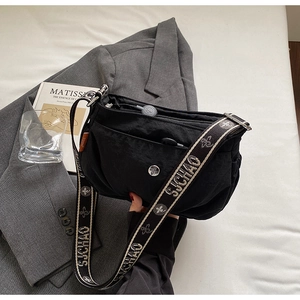 Close-up of black nylon crossbody bag with wide logo strap on grey blazer background