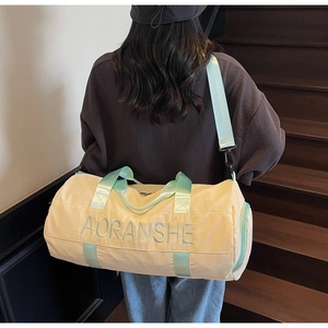 Rear view of a model carrying a beige canvas duffel bag with green straps on stairs