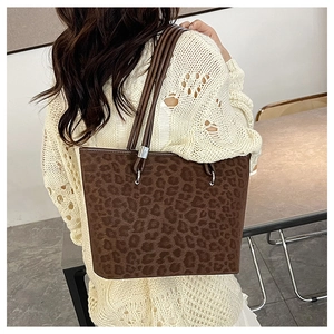Dettaglio borsa shopper leopardata con fibbie metalliche indossata su maglia avorio