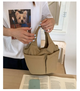 Detail of khaki canvas bucket bag featuring dual front pockets and wide shoulder strap