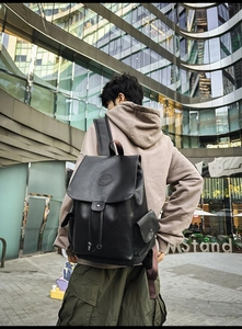Detailed view of a black faux leather backpack with metallic buckle on a male model