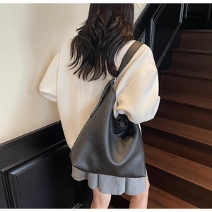 Detail of black pebbled leather texture and wide shoulder strap on large hobo bag
