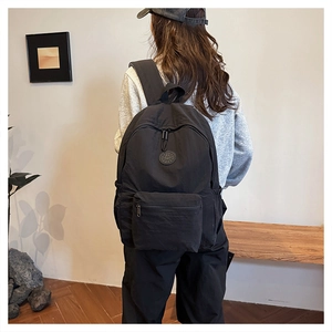 Gros plan d'un sac à dos noir en nylon avec patch logo rond porté sur le dos d'un modèle