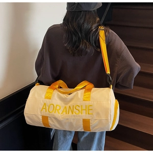 Detail of a beige duffel bag with yellow straps and logo, carried by a model on stairs