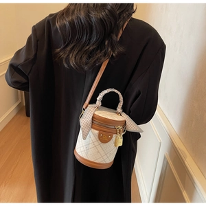 Chic quilted bucket bag with silk scarf handle detail worn by a model in a warm room