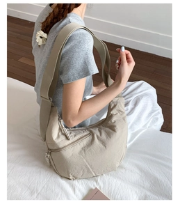 Detail showing the beige nylon crescent bag with wide shoulder strap and zip pocket