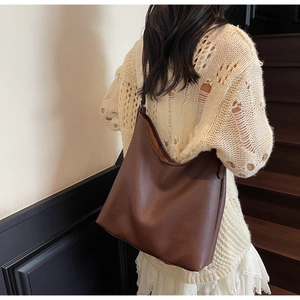 Detail of dark brown pebble leather tote bag shown worn over the shoulder in lifestyle setting