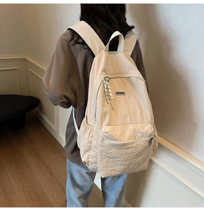Detail of cream nylon backpack with MACHUGE logo and woven zipper pulls on back