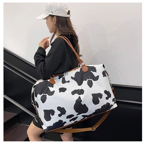 Detail view of large cow print travel bag with brown leather handles worn by a model