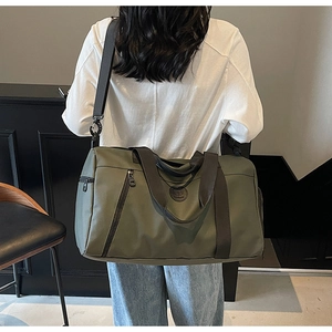 Olive green travel bag detail with black straps shown worn by a model in interior