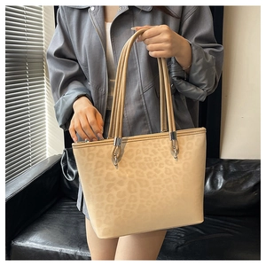 Dettaglio della borsa tote leopardata con attacchi in metallo argentato su superficie beige