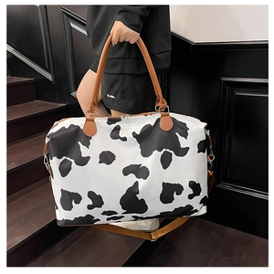 Close-up of a large cow print travel bag with brown leather handles on dark stairs