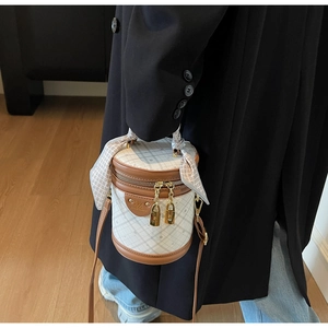 Detail of quilted beige bucket bag with dark brown trim and decorative silk scarf handle