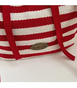 Detail of red and white striped canvas bag with bronze handmade metal logo and fabric handle