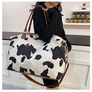 Large travel duffel bag with black and white cow print and brown adjustable shoulder strap