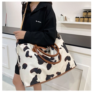 Detail of a large cow print travel bag with leather handles and an adjustable shoulder strap