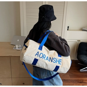 Modern cylinder travel duffel bag with blue webbing straps shown in indoor lifestyle setting