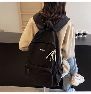 Detail view of the black minimalist backpack featuring a braided zipper puller and side pockets