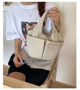 Detail of off-white nylon tote bag with two front pockets shown in hand by model