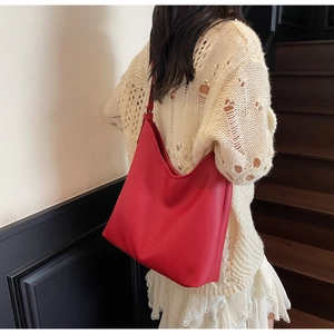 Close-up of a red litchi texture tote bag worn by a model on a shoulder strap